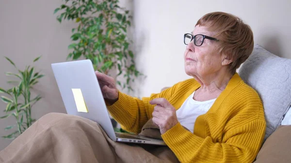 Бабушка использует ноутбук компьютер релаксации в постели. Вычислительные услуги для пенсионеров . — стоковое фото