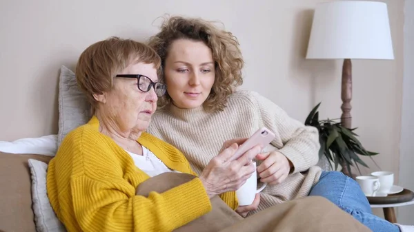 Внучка учит бабушку пользоваться смартфоном дома — стоковое фото