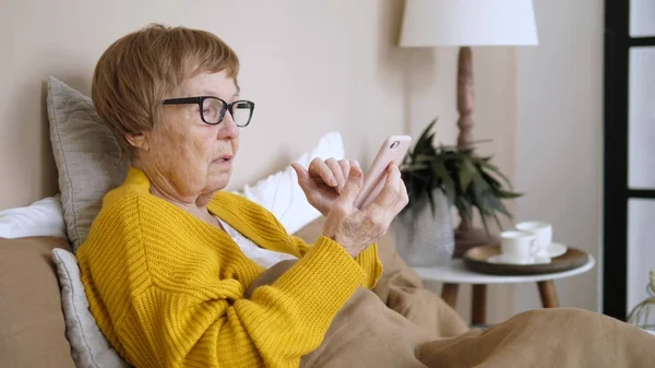 Grootmoeder met behulp van mobiele telefoon rusten thuis in bed — Stockfoto