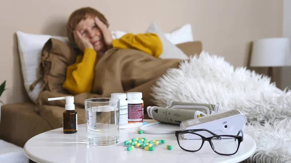 Больная старуха лежит в постели с лекарством и стаканом воды на столе — стоковое фото
