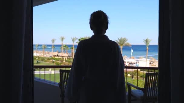 Жінка йде на балконі з видом на море і вдихає зранку. — стокове відео