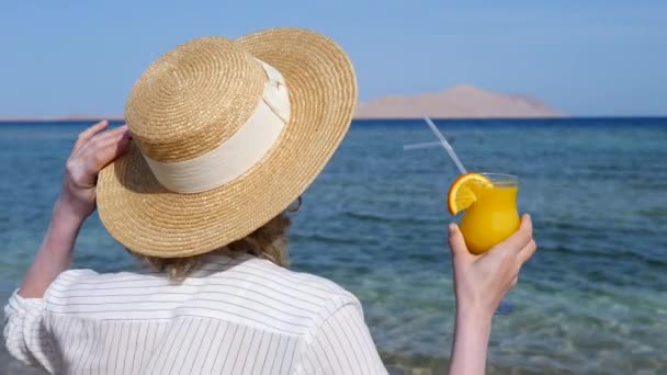 Donna in cappello di paglia che tiene succo d'arancia fresco in spiaggia in vacanza . — Video Stock