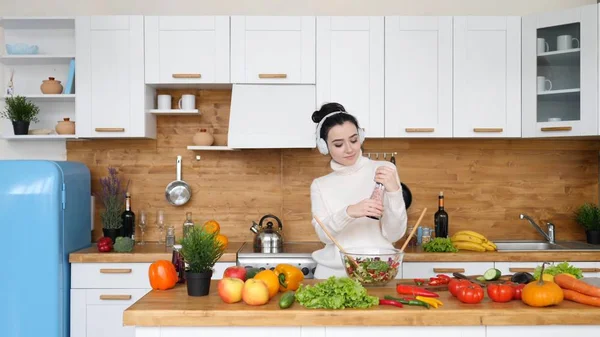 Mujer escuchando música usando auriculares y bailando en la cocina mientras cocina . — Foto de Stock