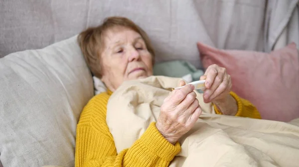 Femme âgée vérifiant la température sur le thermomètre couché dans le lit — Photo