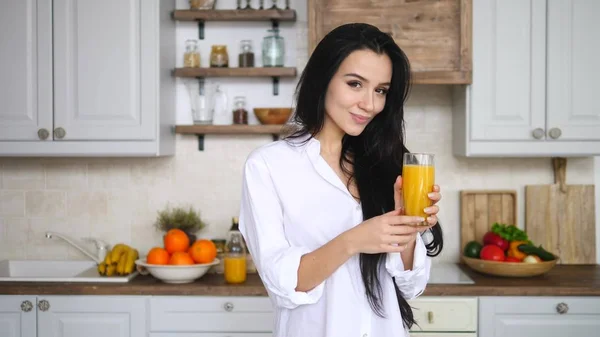 Jovem mulher sorrindo com um copo de suco de laranja fresco na cozinha — Fotografia de Stock