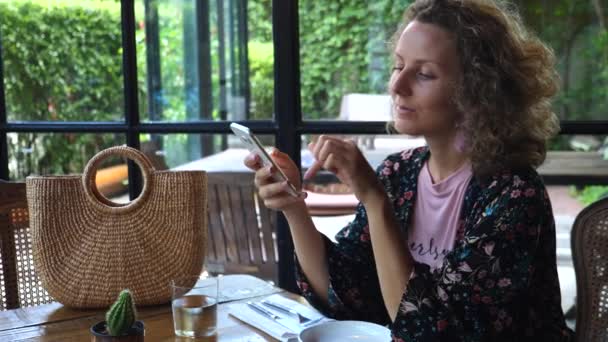 Mujer joven usando el teléfono inteligente en la cafetería — Vídeo de stock