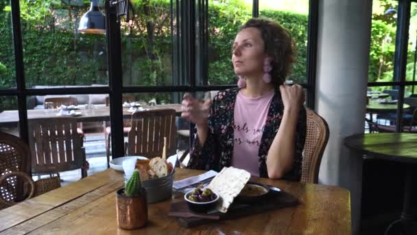 Jonge vrouw zitten in restaurant dineren uitkijken uit het raam — Stockvideo