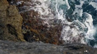 Mavi denizde dalgalar yavaş çekimde kayalara çarpıyor.