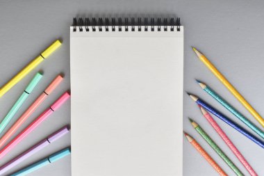 Libreta blanca con lapices y marcadores de colores sobre fondo gris