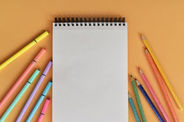 Libreta blanca con lapices y marcadores de colores sobre fondo pastel