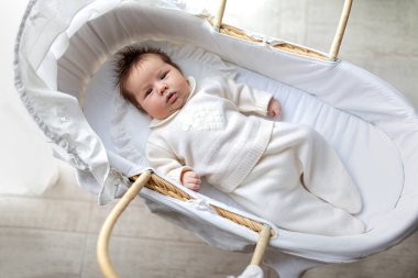 Beyaz pijamalı, yeni doğmuş şirin bir çocuk pipetle beşikte uzanıyor ve beyaz bir battaniyenin üzerindeki kameraya bakıyor. Beşiğinde yeni uyanmış mutlu bir bebek. Üç aylık erkek bebek sırt üstü yatıyor.