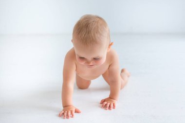 Bebek beyaz bir arka planda sürünüyor. Evdeki temizliği diyorum. Çocuk kameraya bakmıyor.