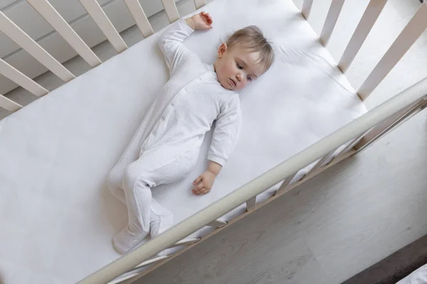 小さな女の子が白いシーツで子供のベッドの中に横たわっているので笑っています テキスト用のスペース 白い背景で スペースのコピー ベッドの上に寝そべってる可愛い赤ちゃん — ストック写真