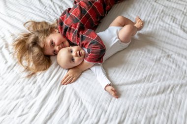 Evdeki küçük mutlu kız kardeşler. Ablası yatakta küçük bebeğe sarılıyor. Kızlar kameraya bakıyor. Yukarıdan manzara. Evde çocuklu bir aile. İki çocuk yatakta yatıyor.