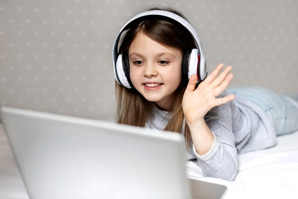 Mutlu kız gülüyor. Çocuk internet üzerinden video bağlantısı ile bir dizüstü bilgisayarla sevinçle iletişim kuruyor. Kovid-19 karantinasında sosyal uzaklık ve kendini izole etme. Evde gülümseyen bir çocuk