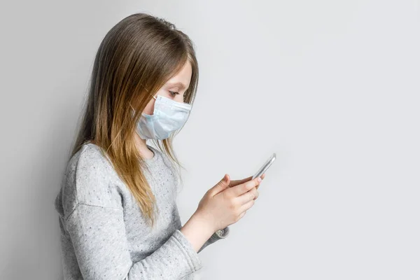 Hijyenik koruyucu maskeli küçük bir kız enfeksiyonu önlemek için elinde telefon tutuyor. Bulaşıcı hastalıklara karşı koruma, koronavirüs. Sağlık ve Tıp Konsepti.