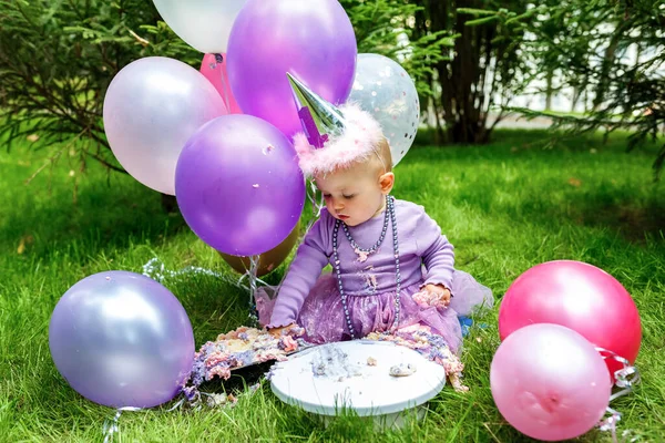 The first birthday of the baby. A small child ridiculously ruins his first cake. One year old baby celebrates birthday in cute dress. Decoration for a baby shower party. Smash cake.