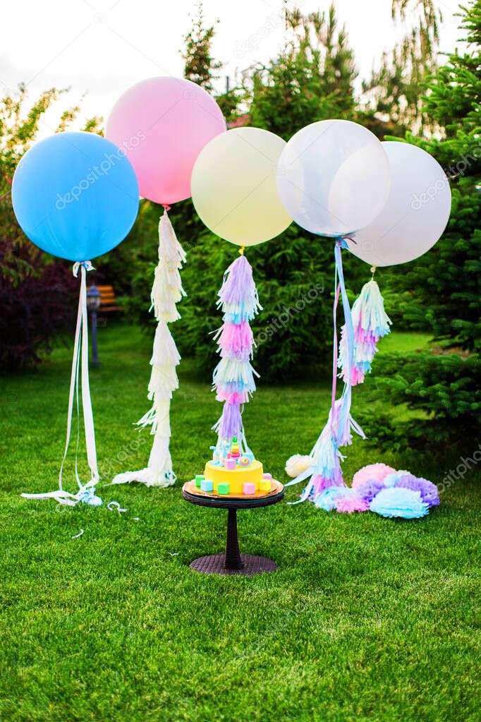Large balloons with helium for a holiday and beautiful cake in summer. Decorations for a birthday party in the nature. Birthday decor in the Park. Summer event.