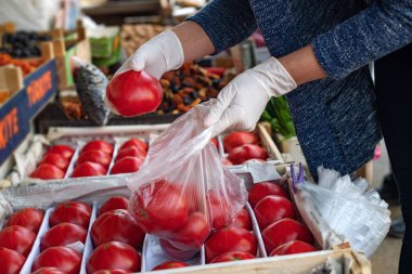 Koronavirüs salgını bağlamında günlük rutin bir uygulama. Güvenli alışveriş kavramı. Aile için ürün almak. Tek kullanımlık eldivenli bir kadın sebze alır.). 
