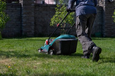 A man with a lawn mower mows the grass. Caring for the backyard. Smooth beautiful green lawn. Gardening/ clipart