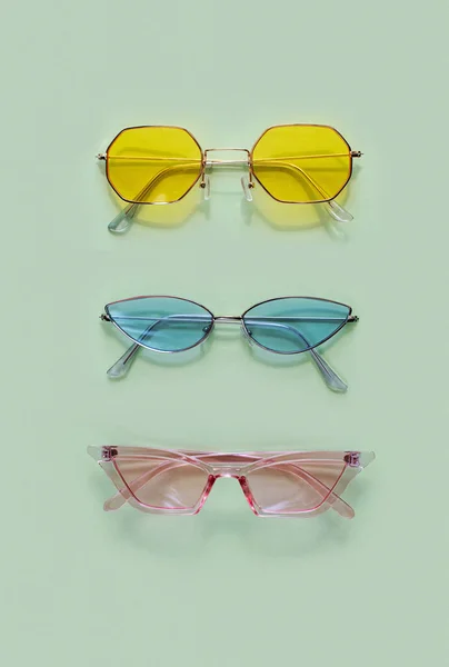 プラスチックフレーム付きのモダンなサングラス 緑の背景に眼鏡で青と黄色のガラス ファッションの眼鏡アクセサリー 夏休みのコンセプト ヒップスタースタイル 柔らかい光の色 ハードシャドウだ ロックダウン — ストック写真