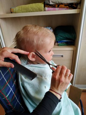 Anne, evdeki banyoda elinde makasla iki yaşındaki oğlu için saçını kestiriyor.