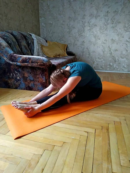 Evinde turuncu yoga minderinin üzerinde gerinen genç bir kadın. — Stok fotoğraf