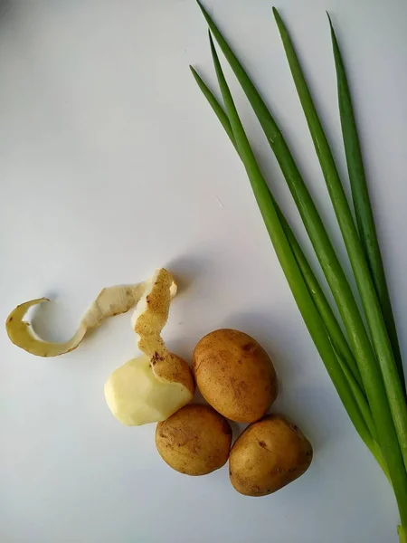 Vier Kartoffeln, eine Hälfte geschält mit frisch geschnittenen grünen Zwiebeln. Vertikales Foto — Stockfoto