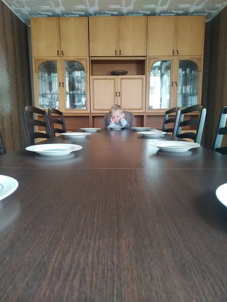 Sad lonely boy sits at an empty huge dining table. loneliness in isolation — Stock Photo, Image