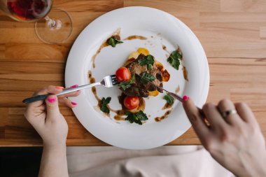 Elinde çatal, elinde bıçak ve bir kadeh şarapla ahşap bir masada sıcak bir tabak. Lezzetli yemekler. Noel yemeği. Lezzetli bir yemek için bir restorana git. Patates ve domatesli sıcak et yemeği. Beyaz tabakta yemek. Çatal ve bıçakla. Yemeğini dışarıda ye.