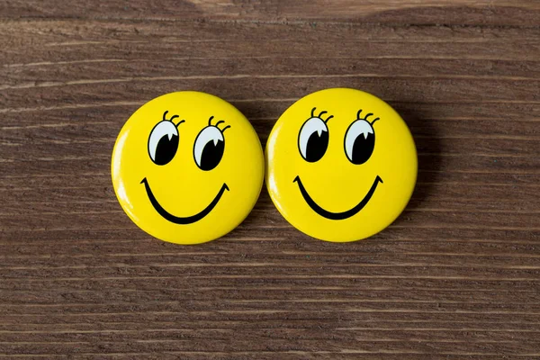 Två gula knappar med leende ansikten på en trä bakgrund. Ovanifrån — Stockfoto