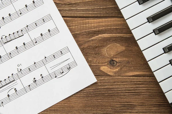 Angled piano keyboard on wooden background with notes — Stock Photo, Image