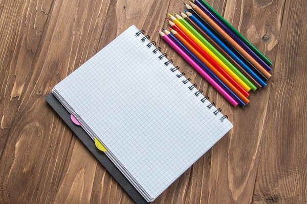 Colored pencils and notepad on wooden background