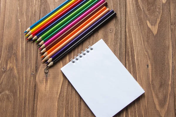 Lápices de colores en la parte superior y bloc de notas sobre fondo de madera — Foto de Stock
