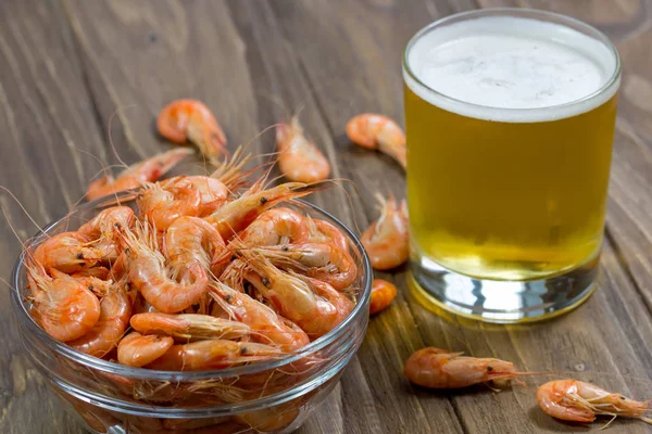 Glass of beer with boiled shrimps in a glass bowl on wooden background — Stock Photo, Image