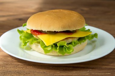 Ahşap arka plan üzerinde beyaz tabakta lezzetli peynirli burger