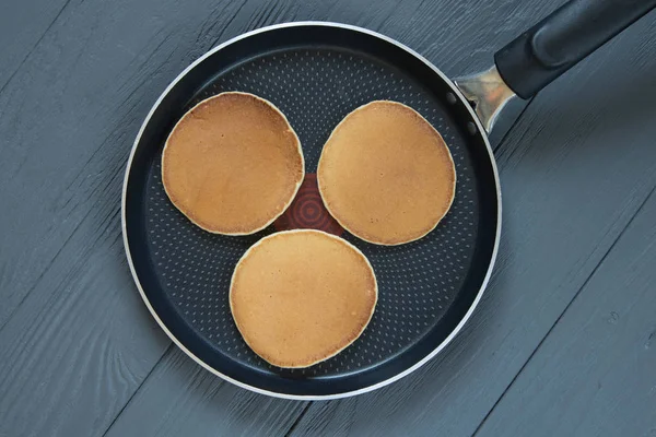 Drei Pfannkuchen in einer Pfanne auf hölzerner Oberfläche — Stockfoto