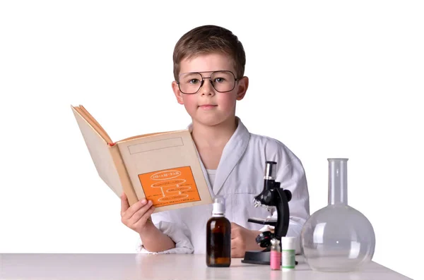 他手里拿着书在桌子上的杯子里科学家男孩 — 图库照片