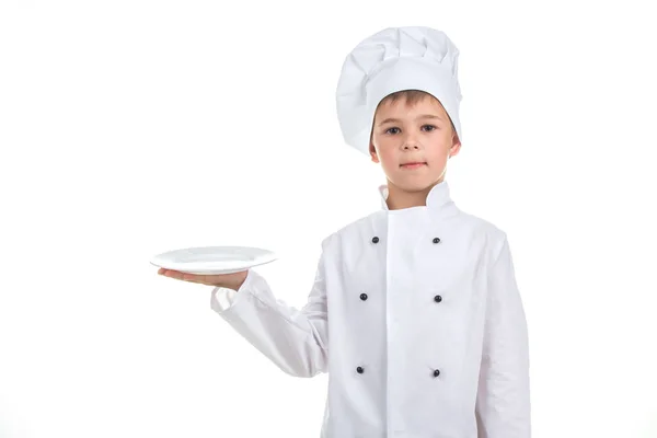 Un gamin avec une assiette vide portant l'uniforme de chef sur fond blanc . — Photo