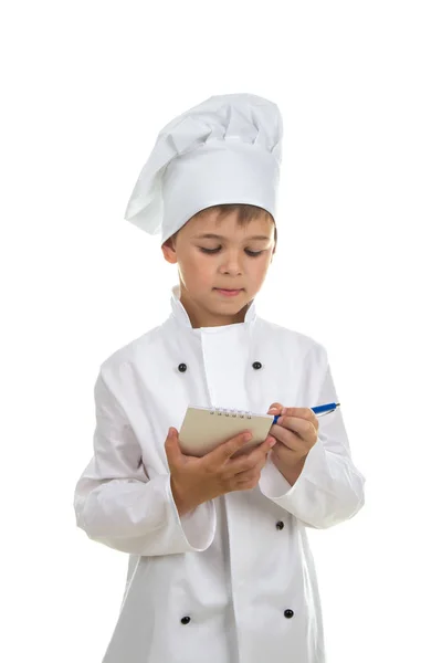 Mały kucharz skoncentrowana zapisuje przepis lub menu. Białe tło. — Zdjęcie stockowe