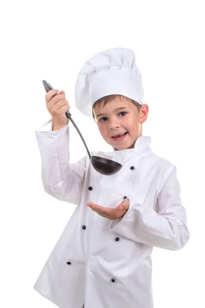 Красивый улыбающийся мальчик в шляпе шеф-повара с ковшами пробует приготовленный бульон . — стоковое фото