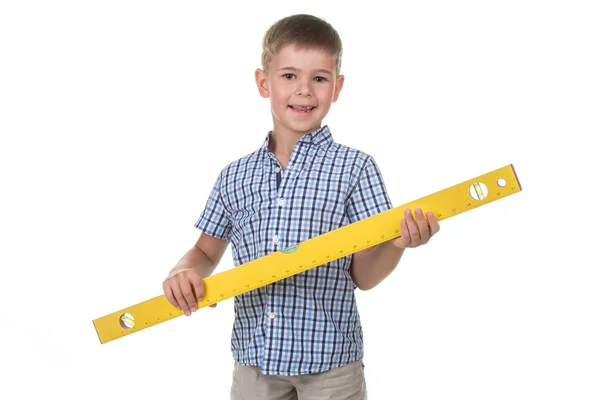 Studio picture of a cute builder boy in a blue checkered shirt, holding a big yellow construction ruler. — Stock Photo, Image