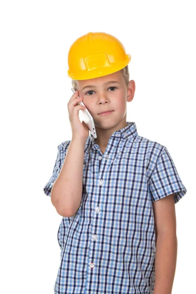 De jongen in de bouwers helm en blauwe geruite shirt spreekt telefonisch, geïsoleerd op witte achtergrond — Stockfoto