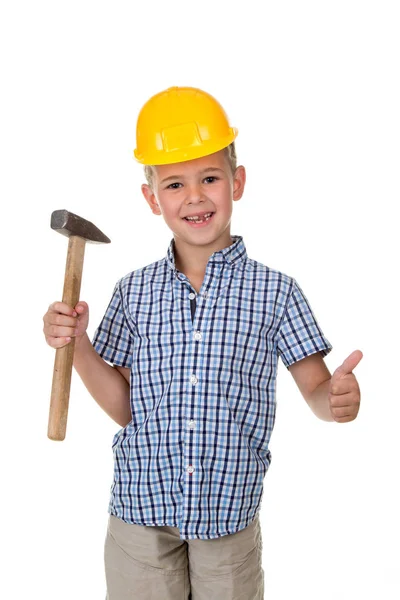 Lindo chico con camisa a cuadros azul y casco de construcción amarillo, sosteniendo un martillo en una mano y mostrando los pulgares hacia arriba — Foto de Stock