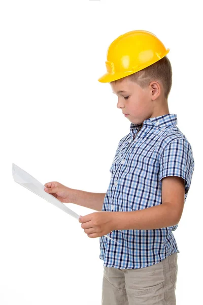 Menino construtor pensativo de chapéu amarelo e camisa quadriculada segurando um plano de papel em suas mãos, isolado em branco — Fotografia de Stock