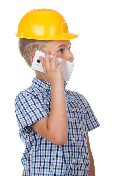 Roztomilý tvůrce chlapec hovoří telefonicky, na sobě žluté protectie helmu a modré kostkované košili. Bílé pozadí. — Stock fotografie