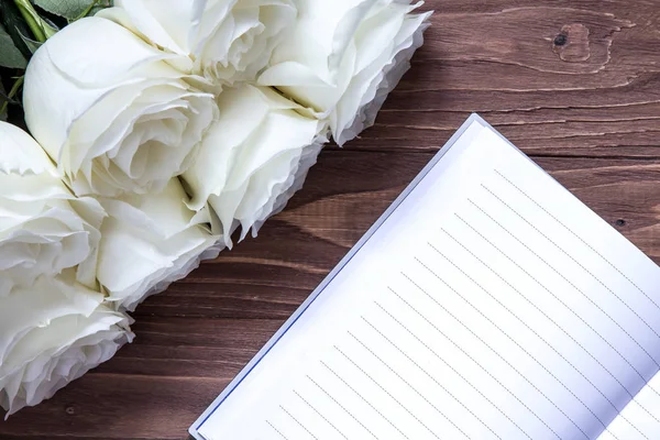 Cuaderno de boda y rosas blancas en la mesa de madera — Foto de Stock