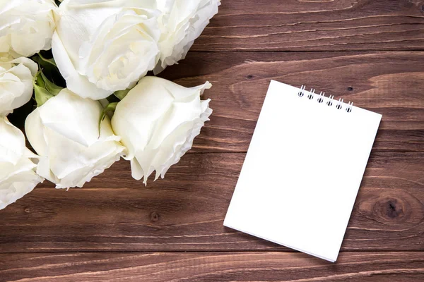 Rosas blancas con papel blanco vacío en la mesa de madera. Fondo de pantalla romántico original para el escritorio — Foto de Stock