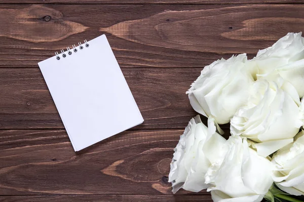 Papel blanco vacío en la mesa de madera. Fondo de pantalla romántico original para el escritorio. Rosas blancas en la esquina derecha del fondo de pantalla de madera — Foto de Stock