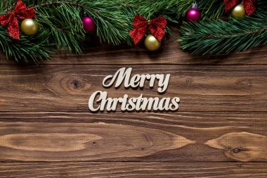 Ekranın üst kısmında çam ağacı ile ahşap arka plan ortasına Merry Christmas dalları